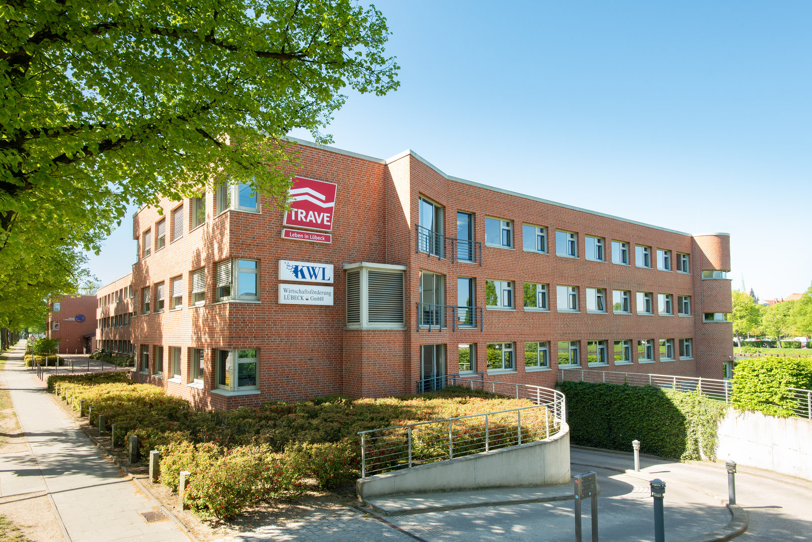 Das Gebäude der TRAVE-Geschäftsstelle in der Falkenstraße 11. Man sieht eine Fensterfront mit dem TRAVE-Logo und die Einfahrt zur Tiefgarage.