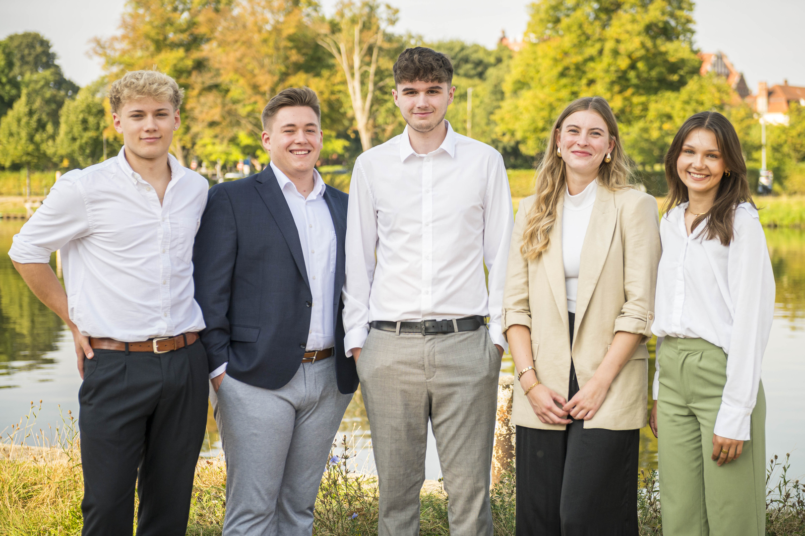 Eine Gruppe von Auszubildenden schaut in die Kamera: Drei junge Männer und zwei junge Frauen aus verschiedenen Ausbildungsjahren stehen am Ufer der Kanaltrave.