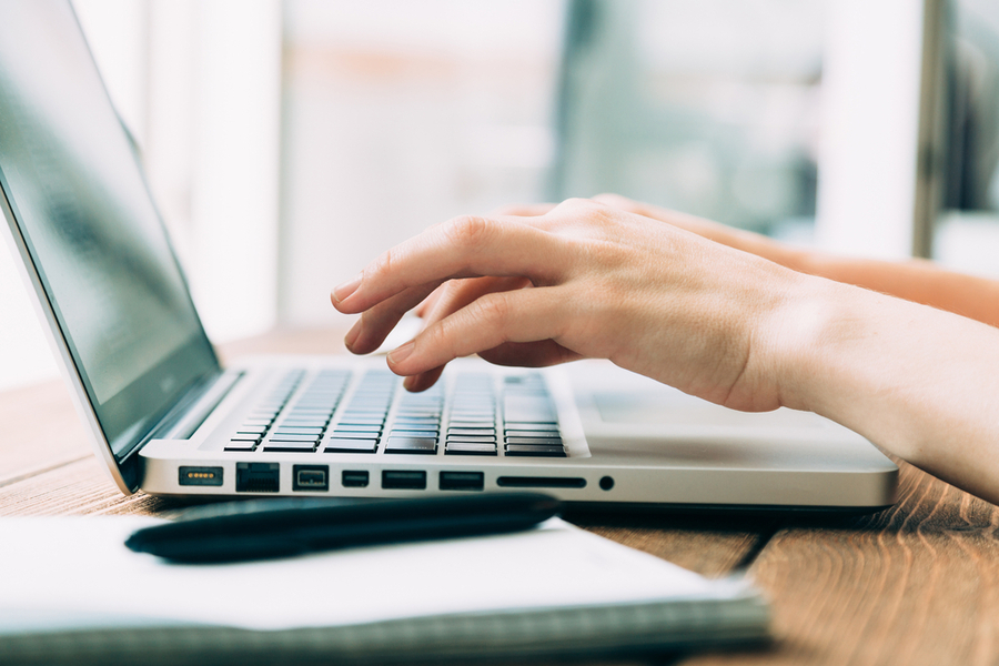 Hände tippen auf einer Laptop-Tastatur neben einem Notizbuch