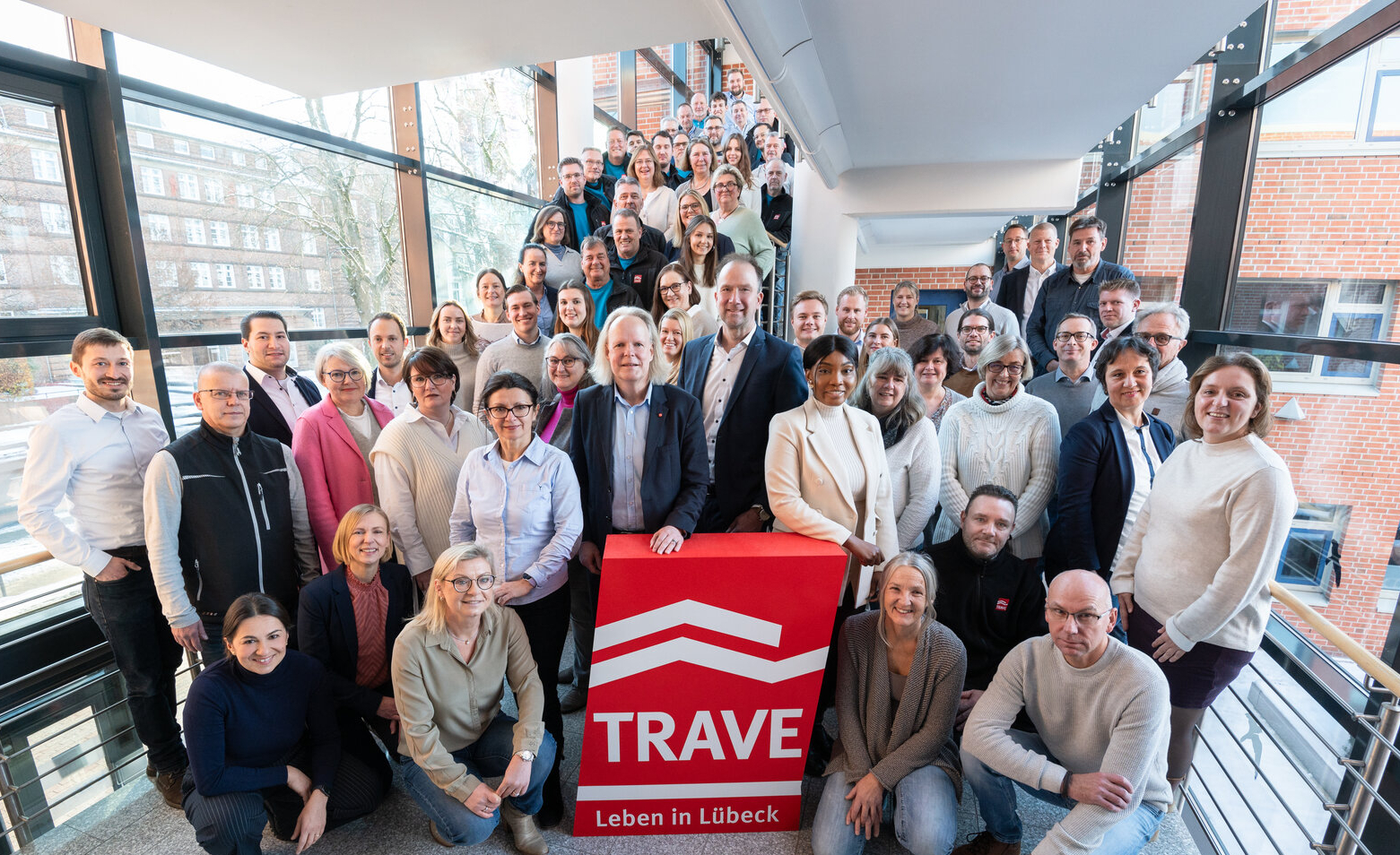 Das TRAVE-Team im Treppenhaus der Falkenstraße 11. Im Vordergrund das TRAVE-Logo und die Geschäftsführer Dr. Matthias Rasch und Sebastian Weist.