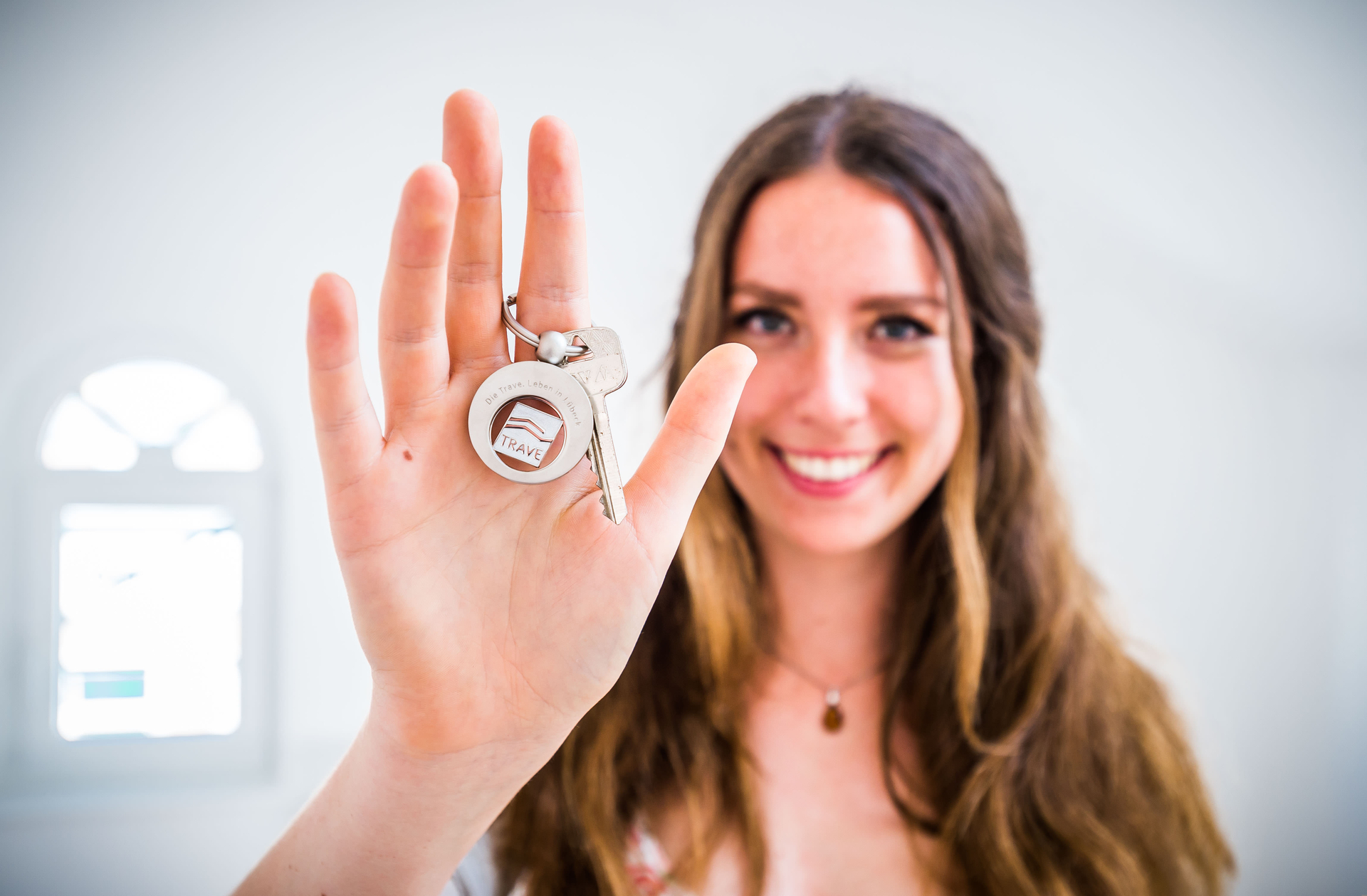 Eine junge Frau hält fröhlich lächelnd einen Schlüsselanhänger der TRAVE in die Kamera.