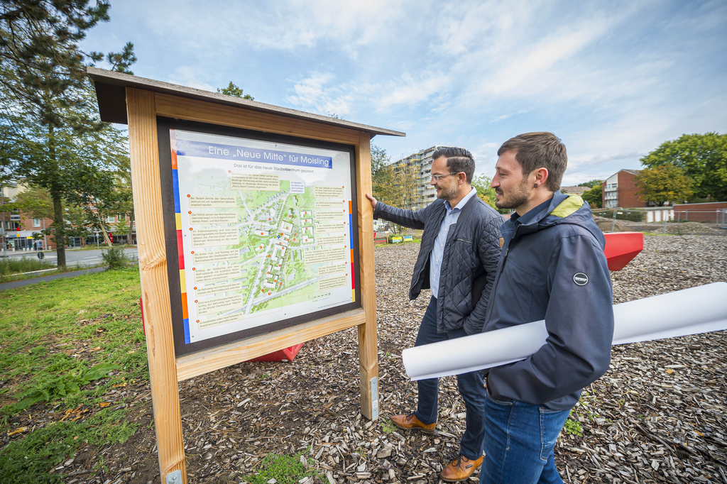Die TRAVE als Sanierungsträger Zwei Männer betrachten eine Informationstafel zu einem Stadtentwicklungsprojekt